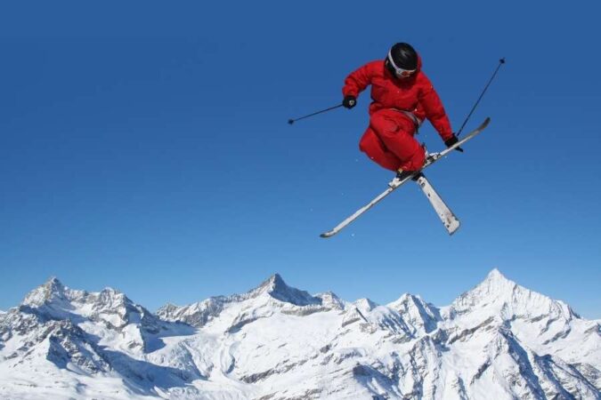 Un skieur en combinaison rouge effectue un saut acrobatique lors d'un voyage au ski avec un panorama de sommets enneigés