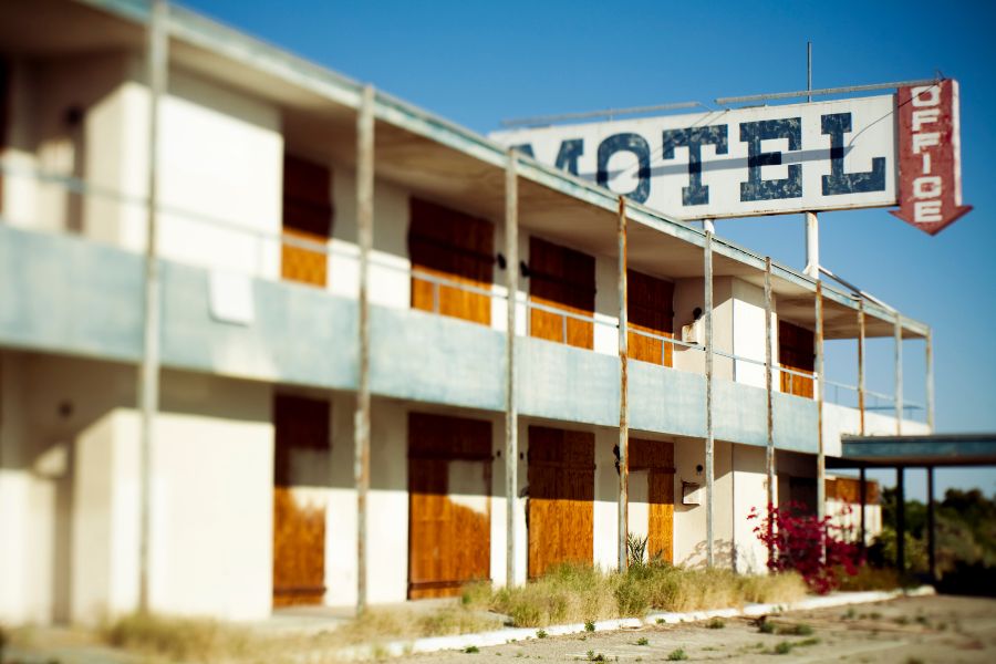 Façade délabrée d'un motel abandonné aux fenêtres condamnées et à l'enseigne usée, sous un ciel bleu méditerranéen.