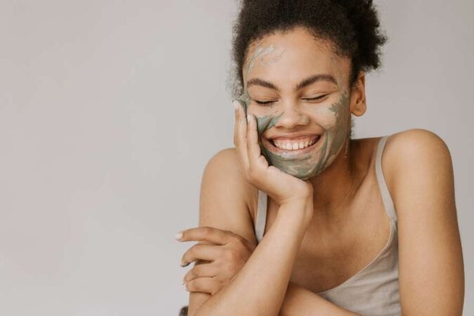 Une jeune femme sourit en appliquant un masque d'argile naturelle lors d'un soin du visage bio.
