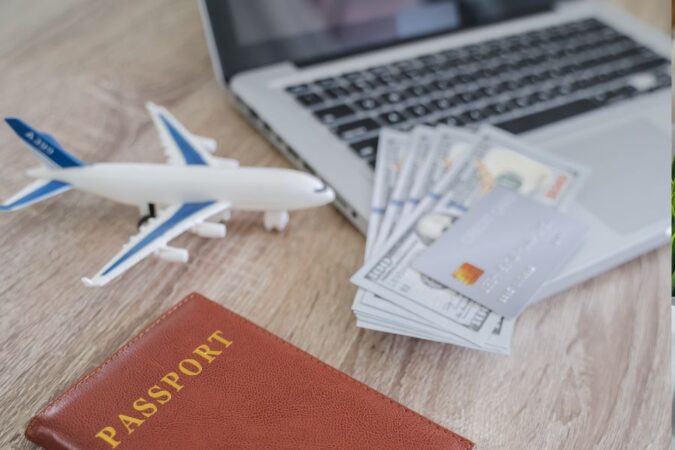Un passeport, des billets de banque et une carte de crédit disposés près d'un ordinateur portable.